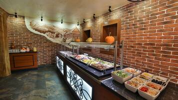 A buffet area with various food options, a brick wall, and a mural of a mountain scene.