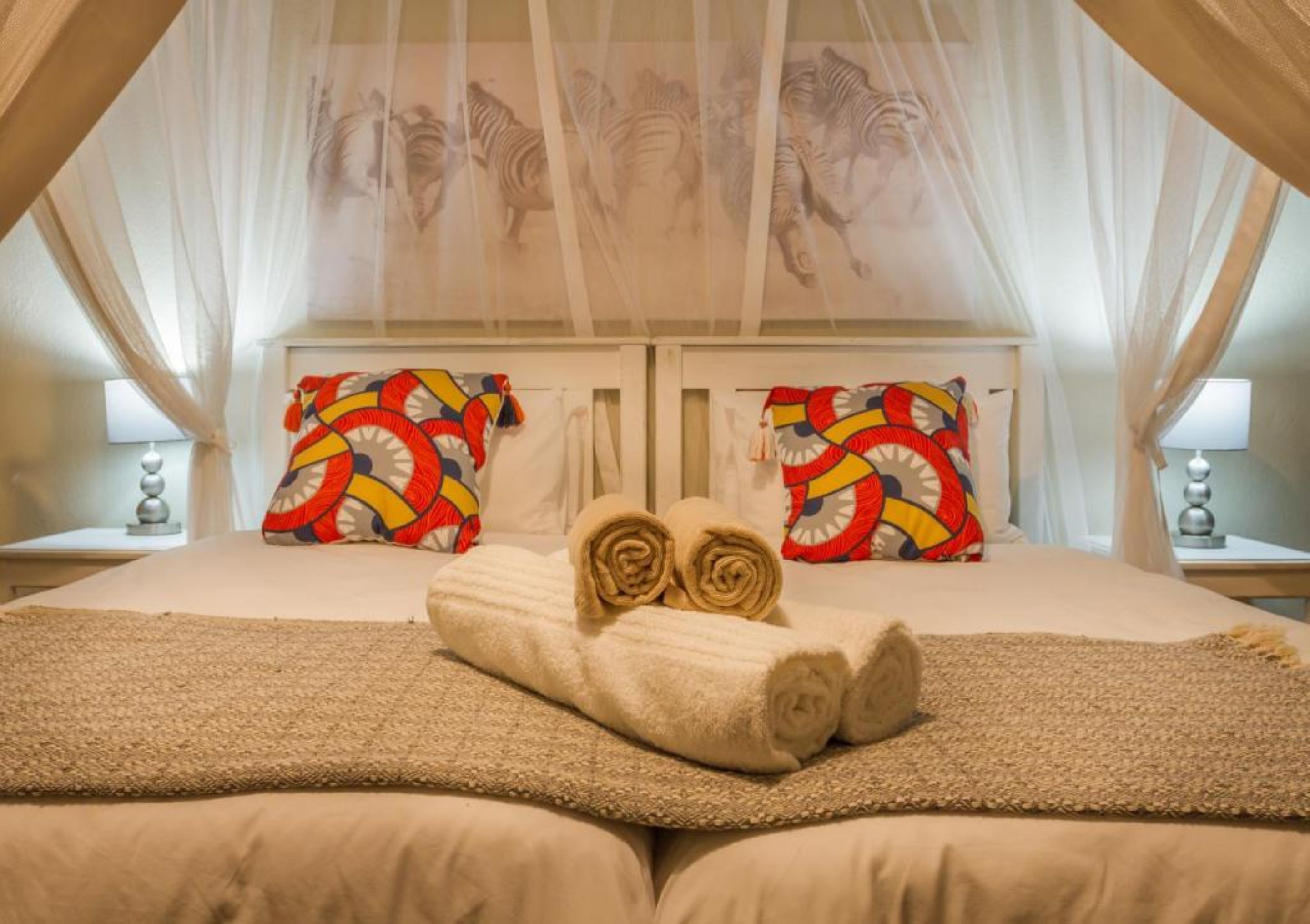 Un dormitorio con cama con dosel, dos mesitas de noche y almohadones estampados.