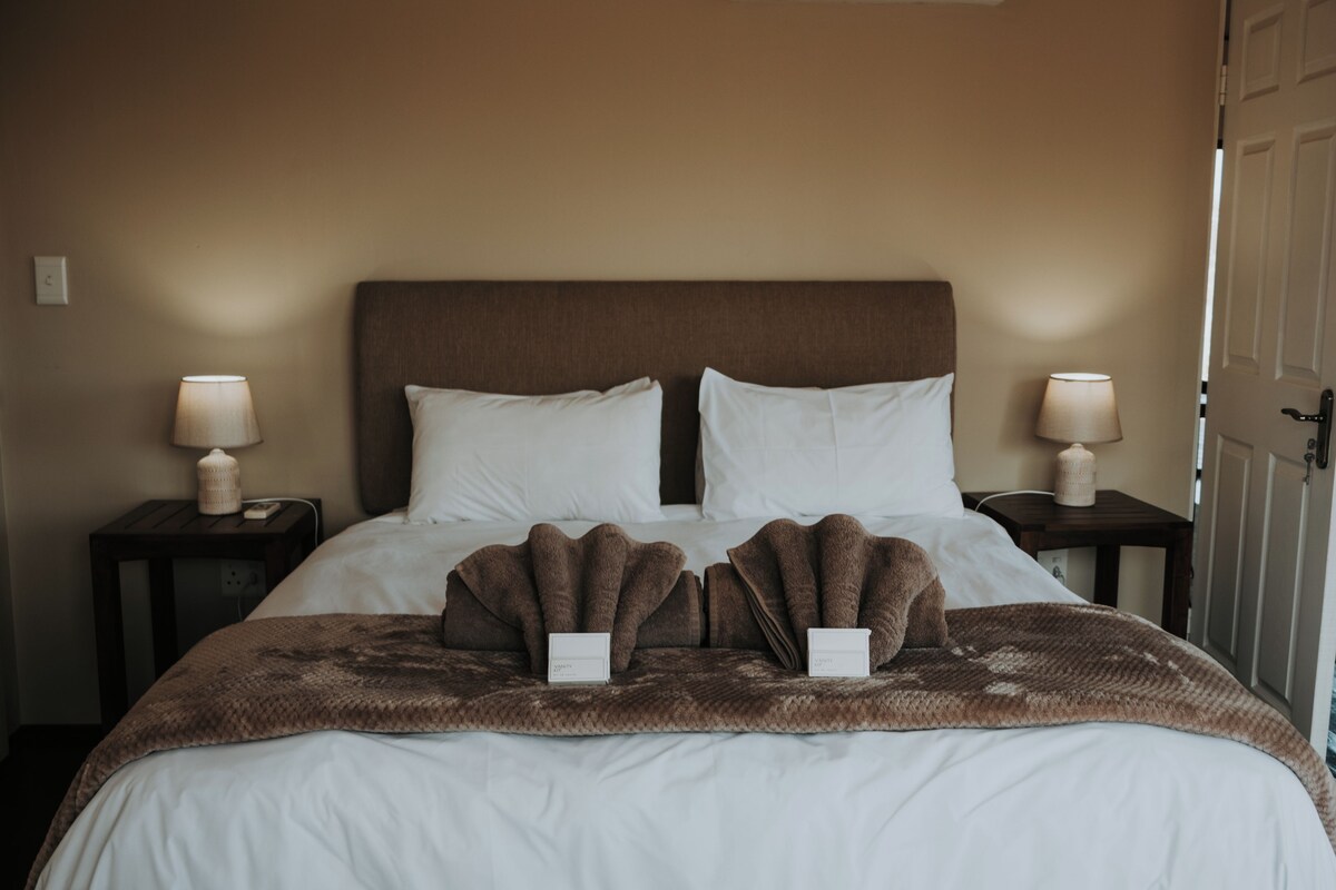 A hotel room with a large bed, two bedside tables, and a door.