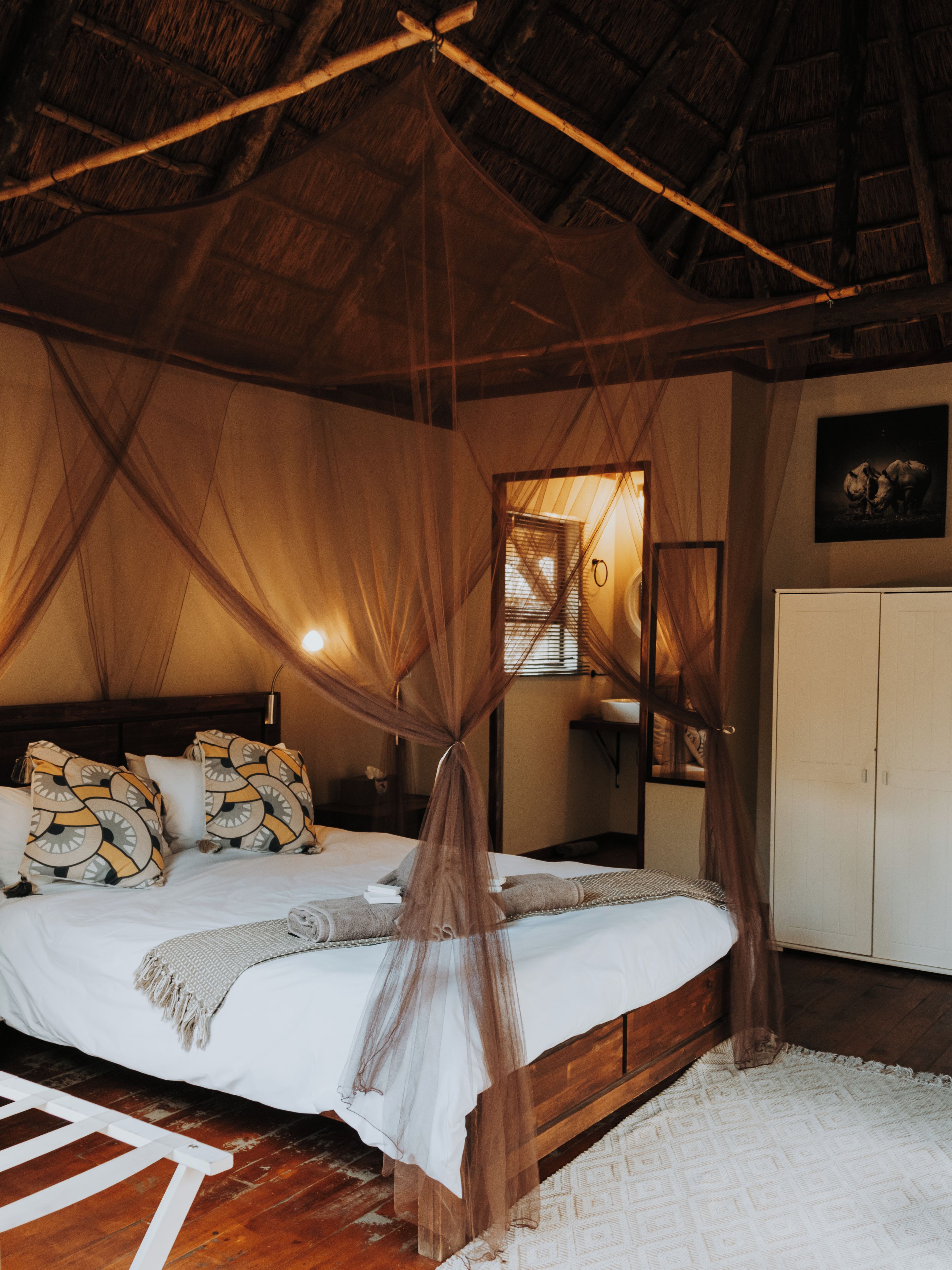 Une chambre à coucher comprenant un lit, une tête de lit en bois, une table de chevet, une armoire et une moustiquaire.