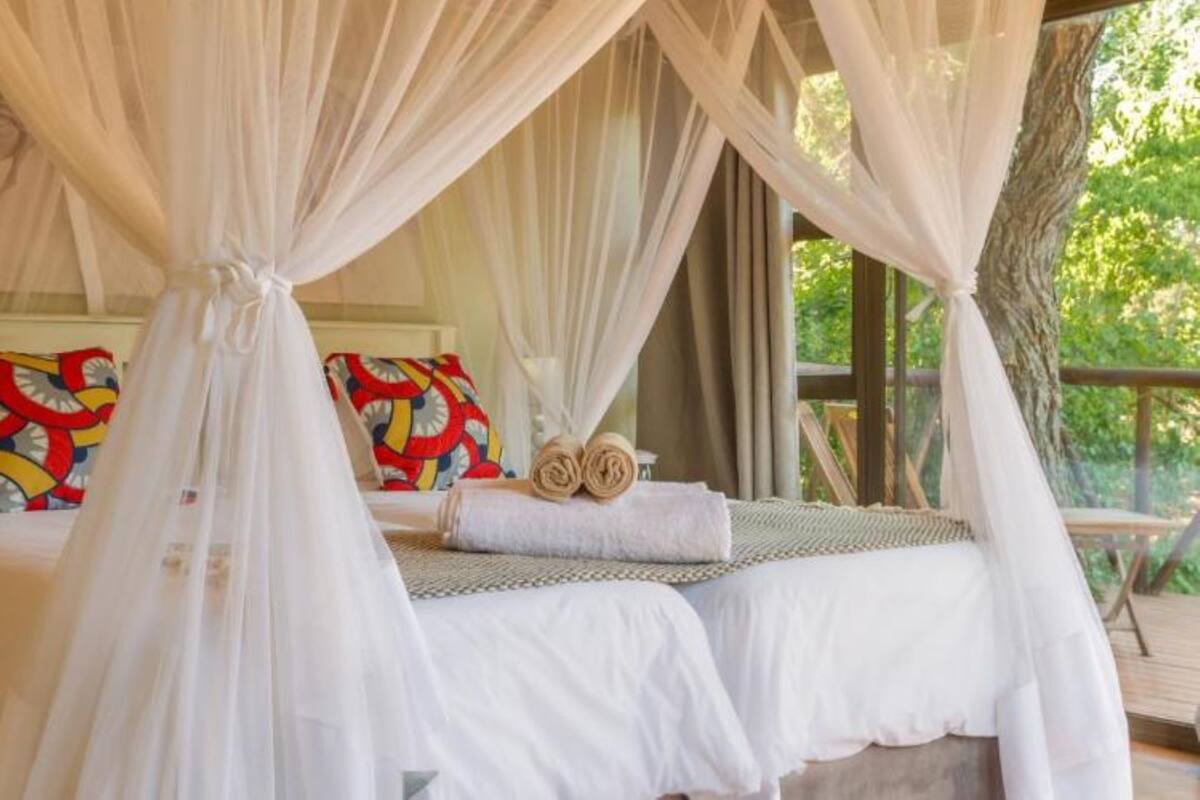 A bedroom with a canopy bed, colorful pillows, and a view of greenery outside.