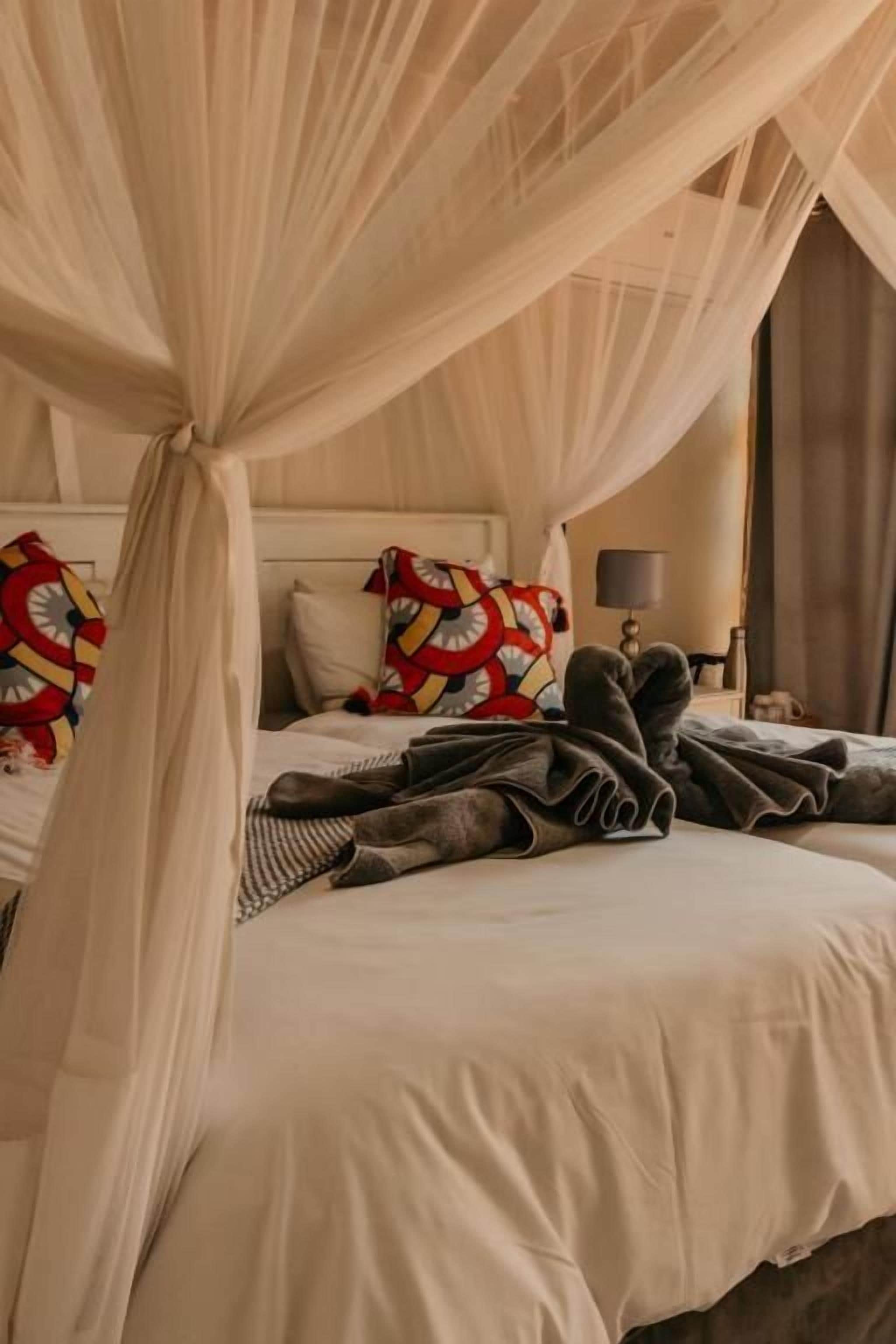 Une chambre à coucher avec un lit à baldaquin, des oreillers à motifs rouges et jaunes, et une table de chevet avec une lampe.
