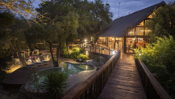 A wooden deck leading to a pool area with lounge chairs and a restaurant.