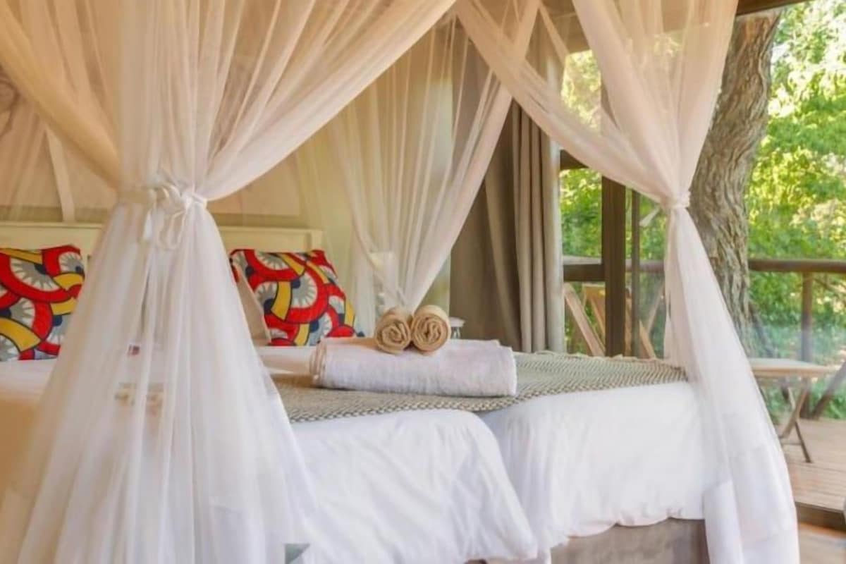 Un dormitorio con cama a dosel, una mesita de noche y una cama con almohadas coloridas.
