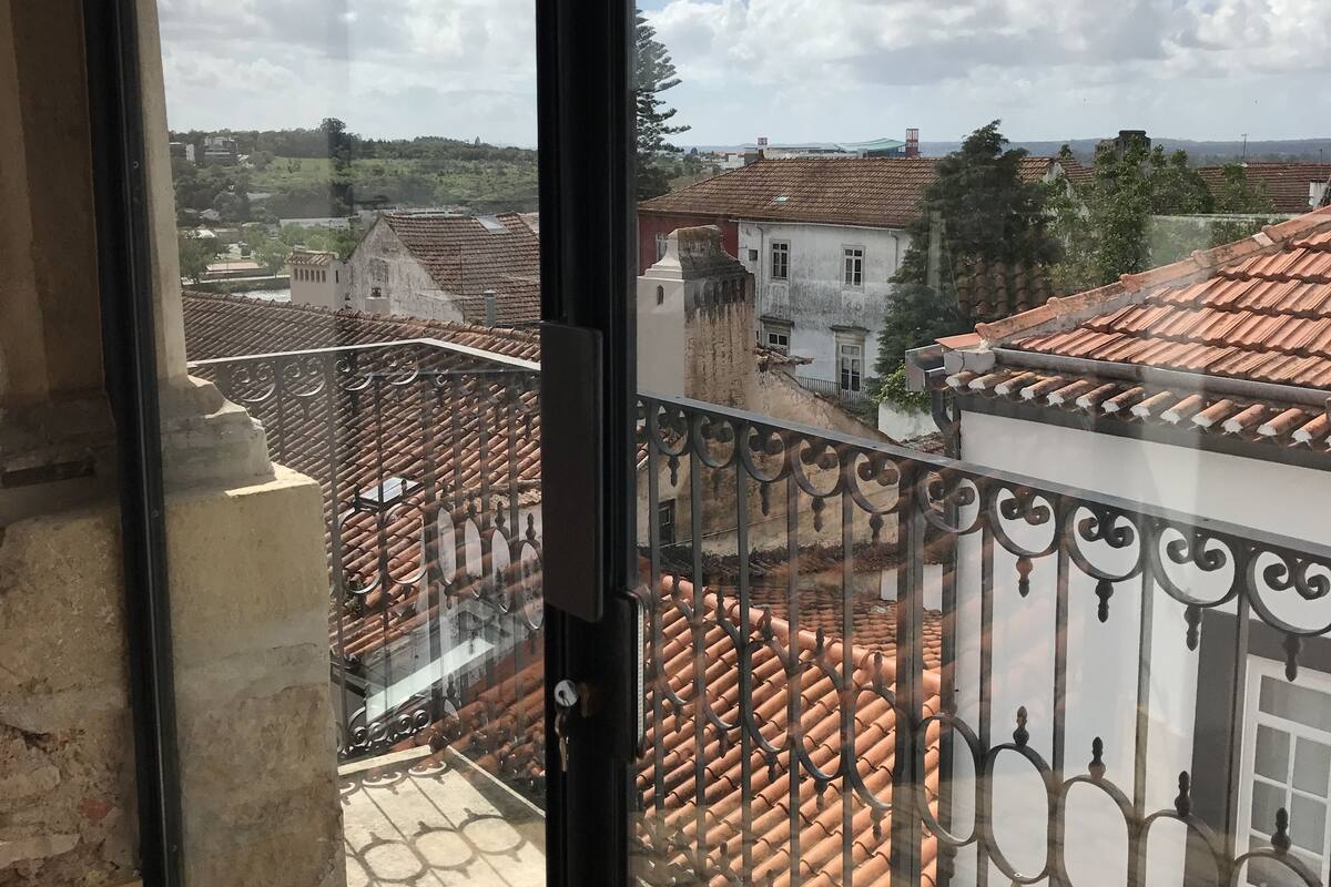 A balcony with a wrought iron railing overlooking a town with terracotta rooftops and a clear sky.