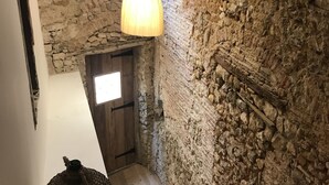 Una scala con una parete in pietra rustica, gradini in legno e un cesto di vimini su un supporto metallico.