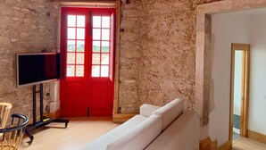 Una stanza con pareti in pietra, una porta rossa, un divano bianco e una TV su un supporto.
