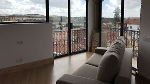 Un ampio balcone con vista sulla città, un'area salotto con cuscini e ampie finestre.