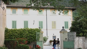 A building with a white facade, green shutters, and a garden with red flowers. - Villa del Cardinale (Spoleto)