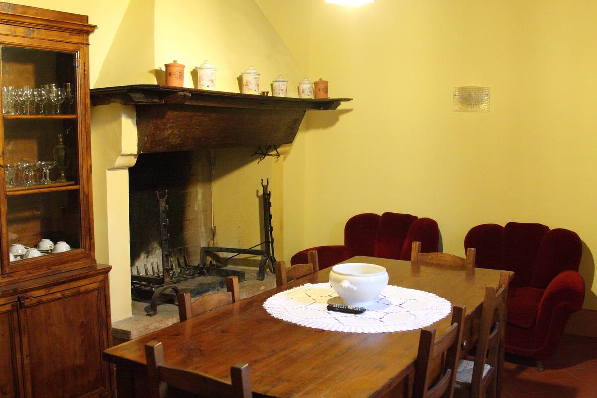 A dining room with a wooden table, red chairs, a white bowl, and a fireplace.
