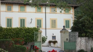 A two-story building with green shutters, a small balcony, and a garden with red flowers and a table. - Villa del Cardinale (Spoleto)
