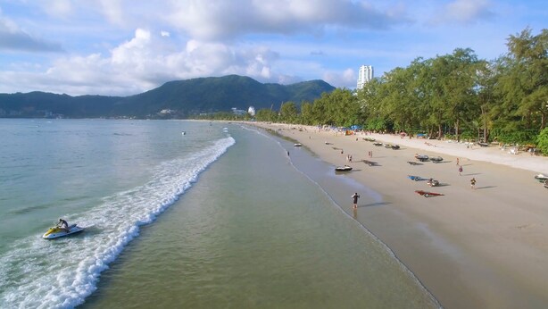 A beach with clear water, a sandy shore, and a line of trees. - Hangover Inn (Patong)