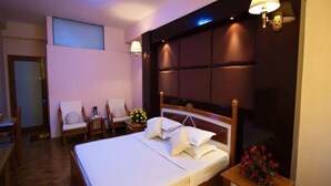 A hotel room with a large bed, two chairs, a nightstand with a vase of flowers, and a wall-mounted lamp. - The Prince Hotel Mandalay (Mandalay)
