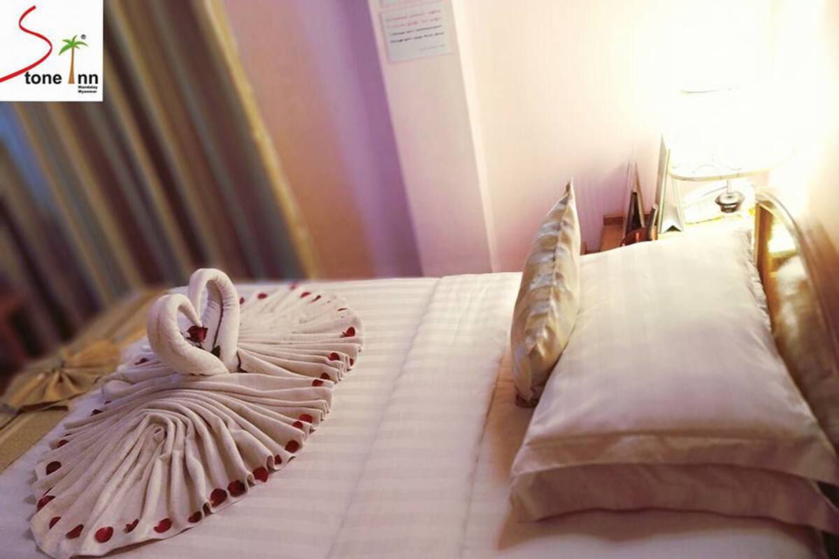 Habitación de hotel con una cama bien hecha, una toalla con forma de cisne y una lámpara en la mesita de noche.