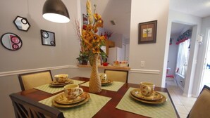 A dining area with a wooden table set for four, surrounded by chairs. There is a decorative vase with sunflowers on the table, and the walls are adorned with framed pictures. - Ly53793 - Indian Ridge - 3 Bed 2 Baths Villa (Kissimmee)