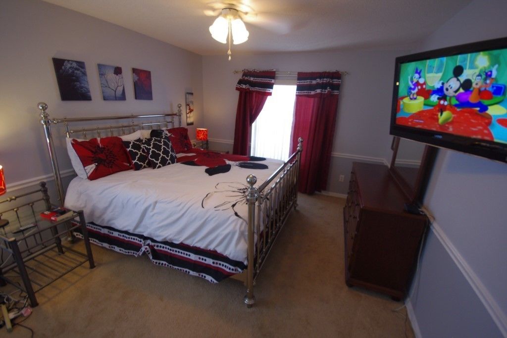 A bedroom with a metal-framed bed, a television on the wall, and a window with red curtains.