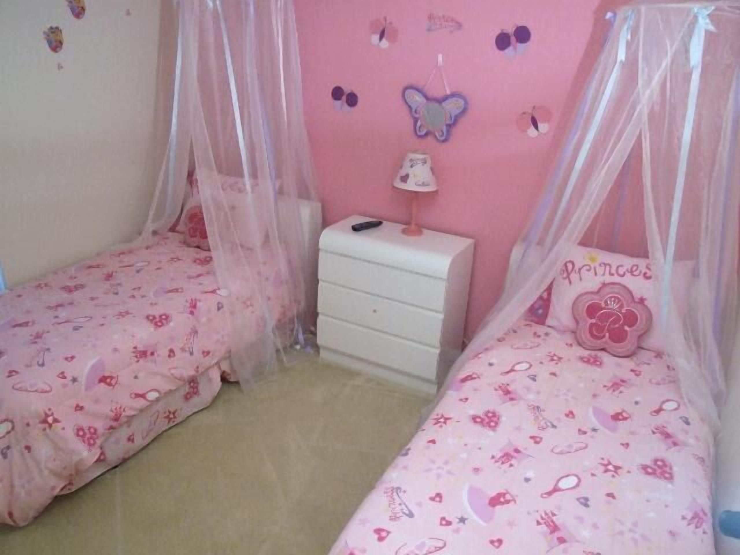 A bedroom with two single beds, a nightstand, a lamp, and a wall decorated with butterfly stickers.