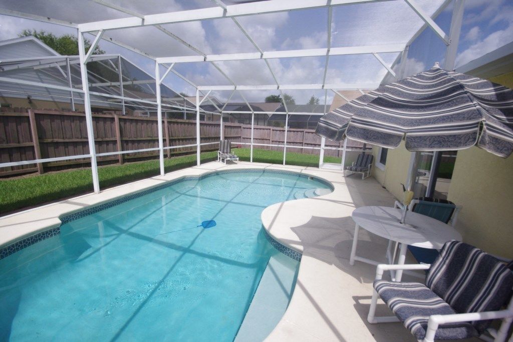Ein überdachter Hinterhof mit Swimmingpool, Gartenmöbeln und Sonnenschirm.