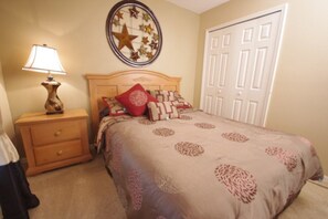 Un dormitorio con cama, mesita de noche, lámpara, decoración en la pared y una puerta.