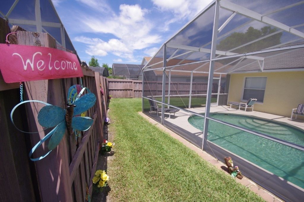 A backyard with a swimming pool, a covered patio, and a 'Welcome' sign.