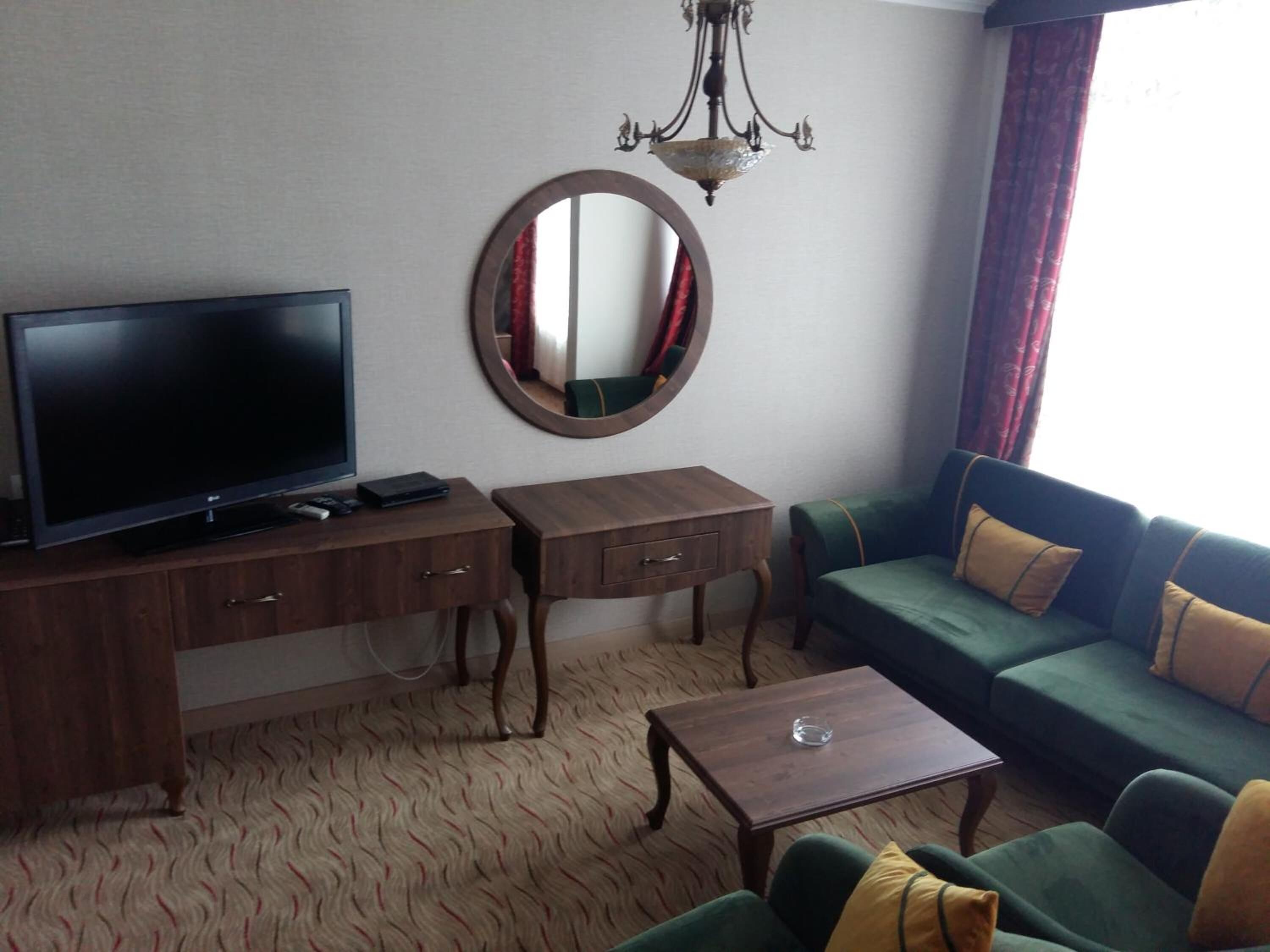 A hotel room with a television, a desk with drawers, a round mirror, a sofa with cushions, and a small table.