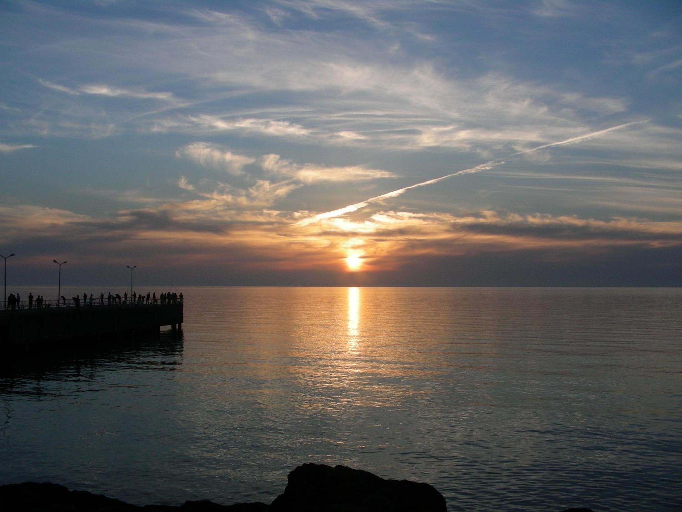 Un coucher de soleil sur une mer calme, avec une jetée qui s’avance dans l’eau.