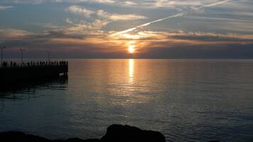 Un coucher de soleil sur une mer calme, avec une jetée qui s’avance dans l’eau.