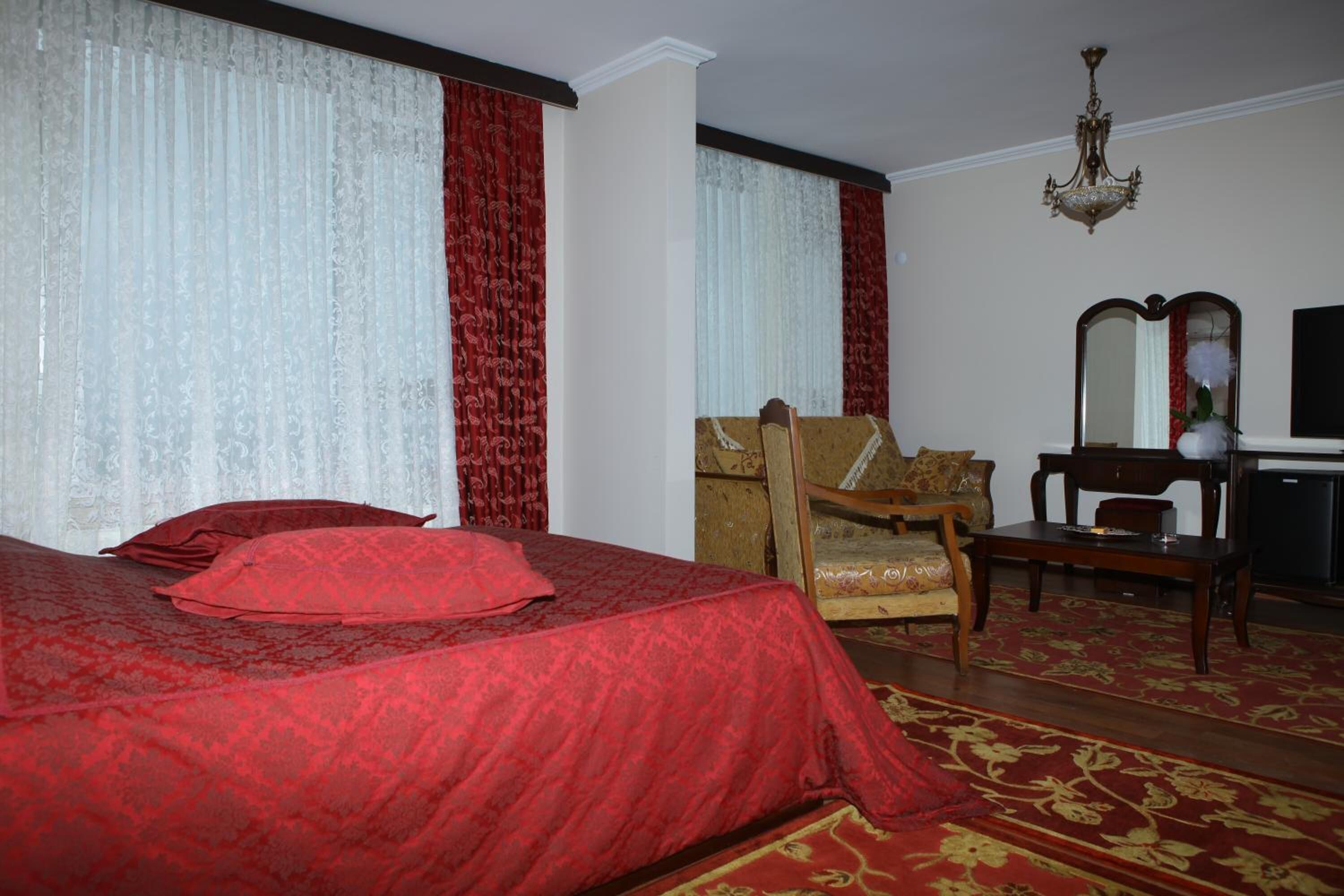 A hotel room with a large bed, a wooden armchair, a desk with a mirror, and a chandelier.