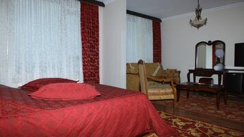 A hotel room with a large bed, a wooden armchair, a desk with a mirror, and a chandelier.