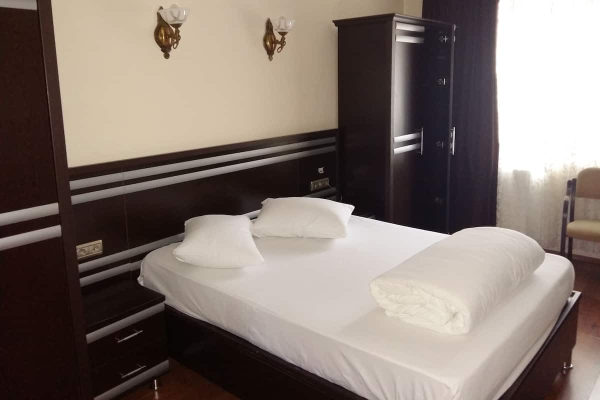 A hotel room with a large bed, two wall sconces, a wardrobe, and a chair.