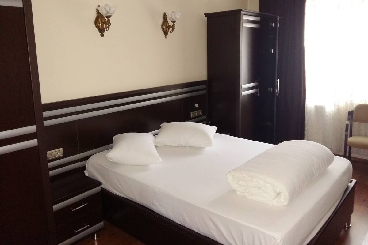 A hotel room with a large bed, a wardrobe, a nightstand, and two wall-mounted lamps.