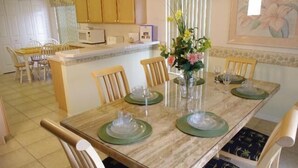 A dining area with a wooden table set for four, surrounded by chairs with dark patterned upholstery. A vase with flowers is placed on the table, and a microwave is visible in the background. - Ly53798 - Indian Ridge - 4 Bed 2 Baths Villa (Kissimmee)