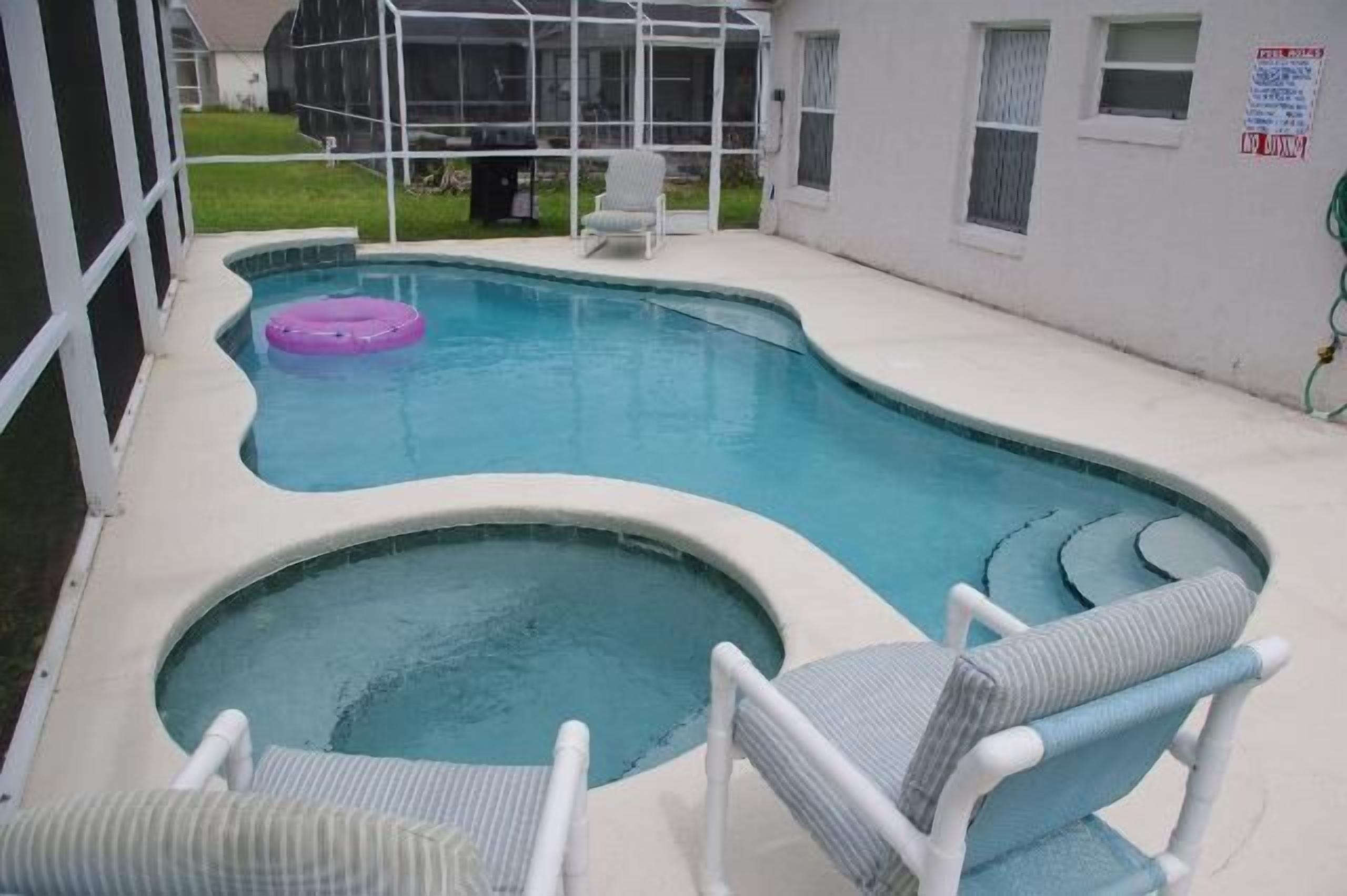 Una piscina con un pequeño jacuzzi, rodeada de sillas blancas y una zona cubierta.