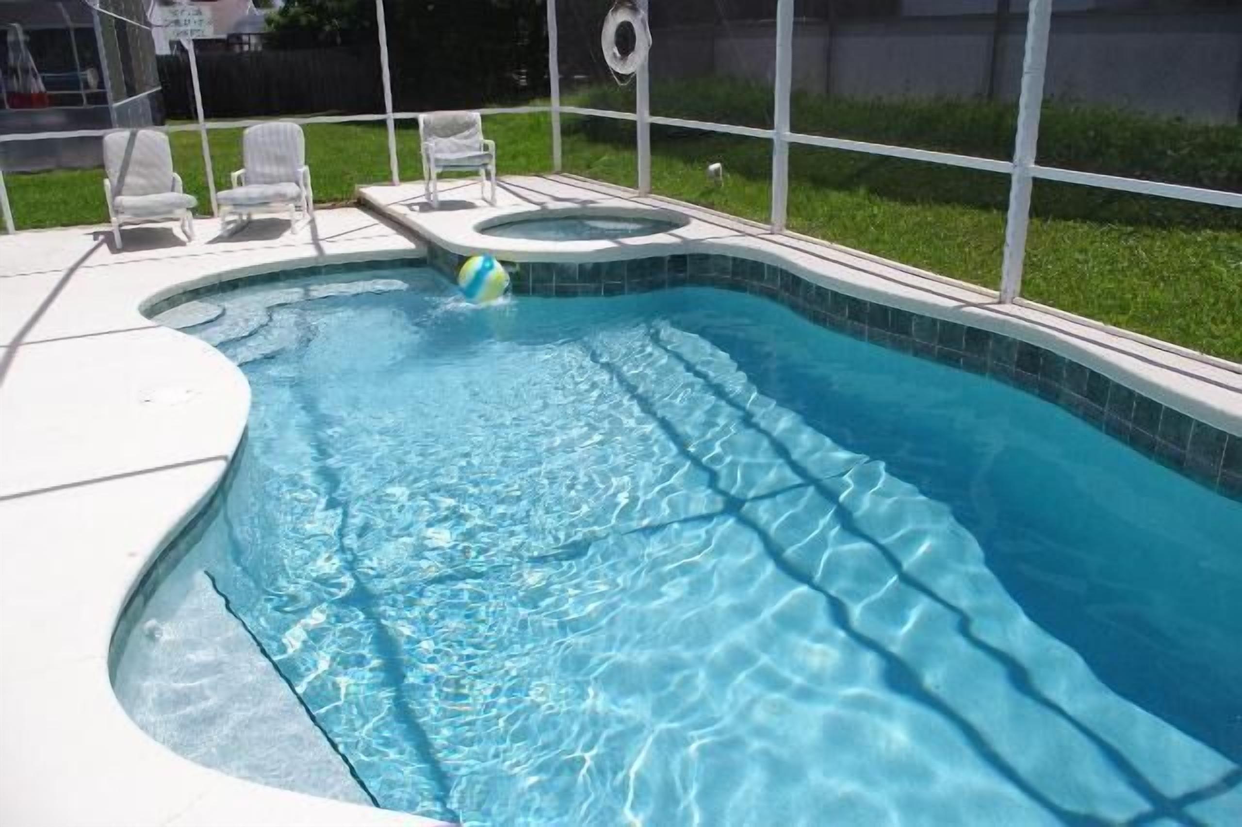 A swimming pool with a hot tub, surrounded by a white fence and a grassy yard.