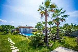 Un patio trasero con piscina, palmeras y una casa.