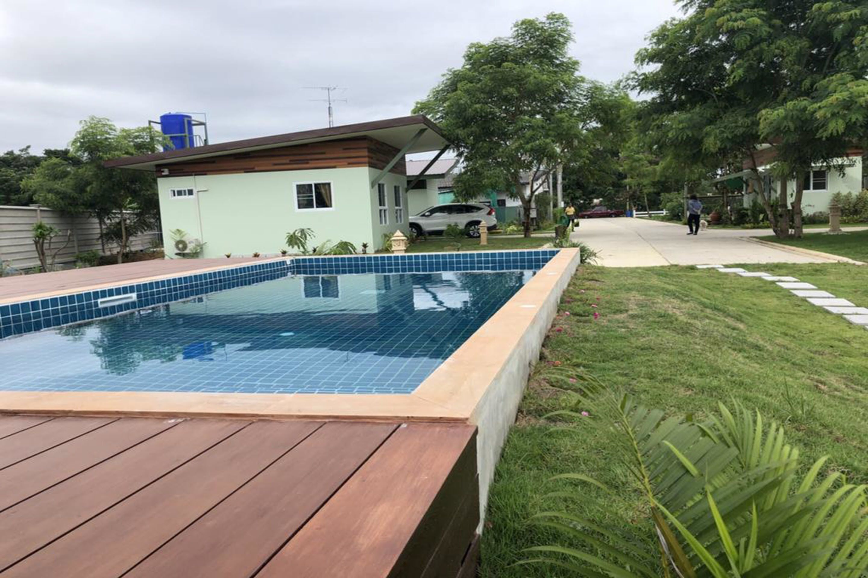A swimming pool with a wooden deck, surrounded by a grassy area and trees.