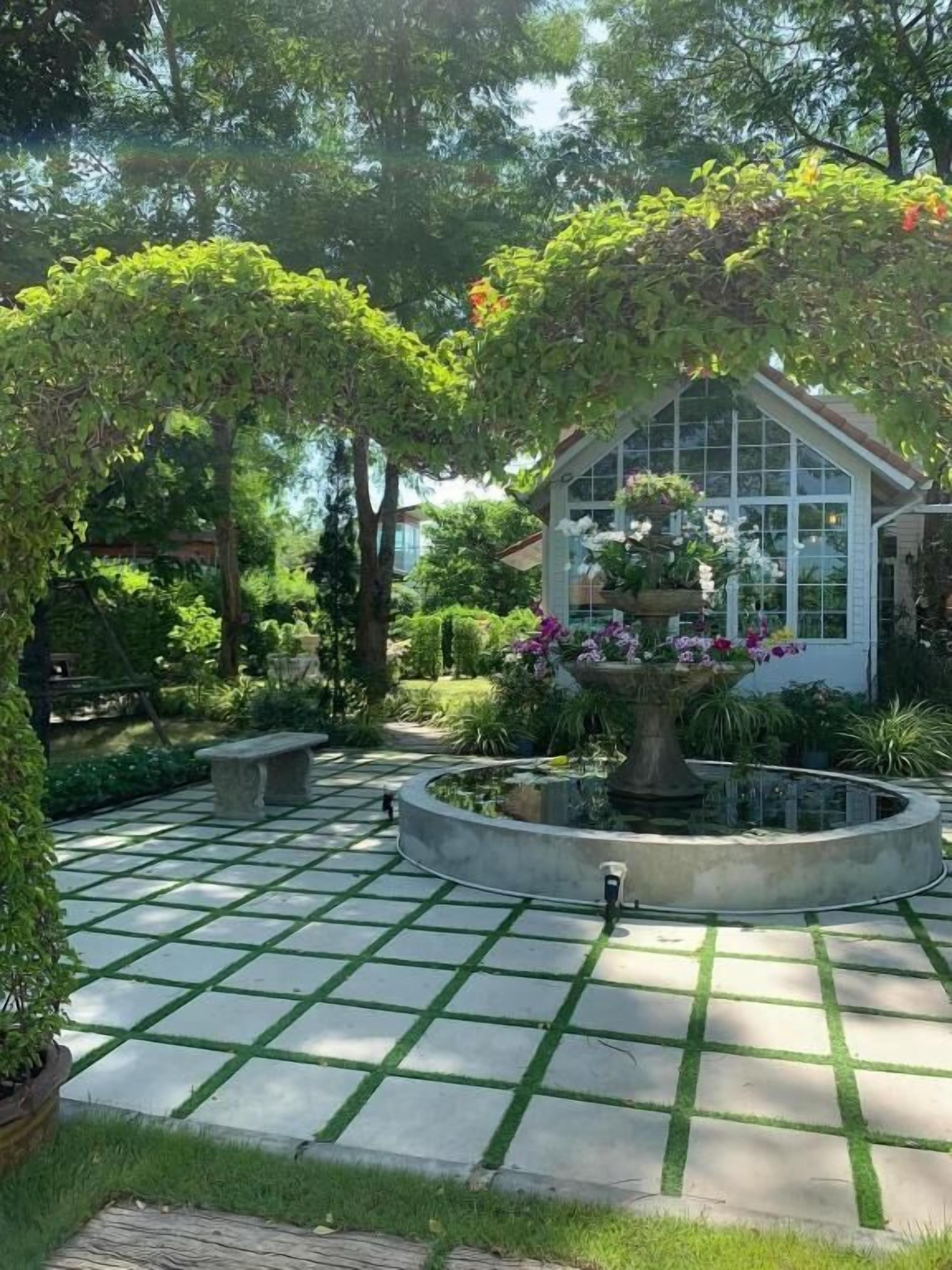 Ein Garten mit einem Brunnen, einem kreisförmigen Steinweg und einem Gebäude mit großen Fenstern.