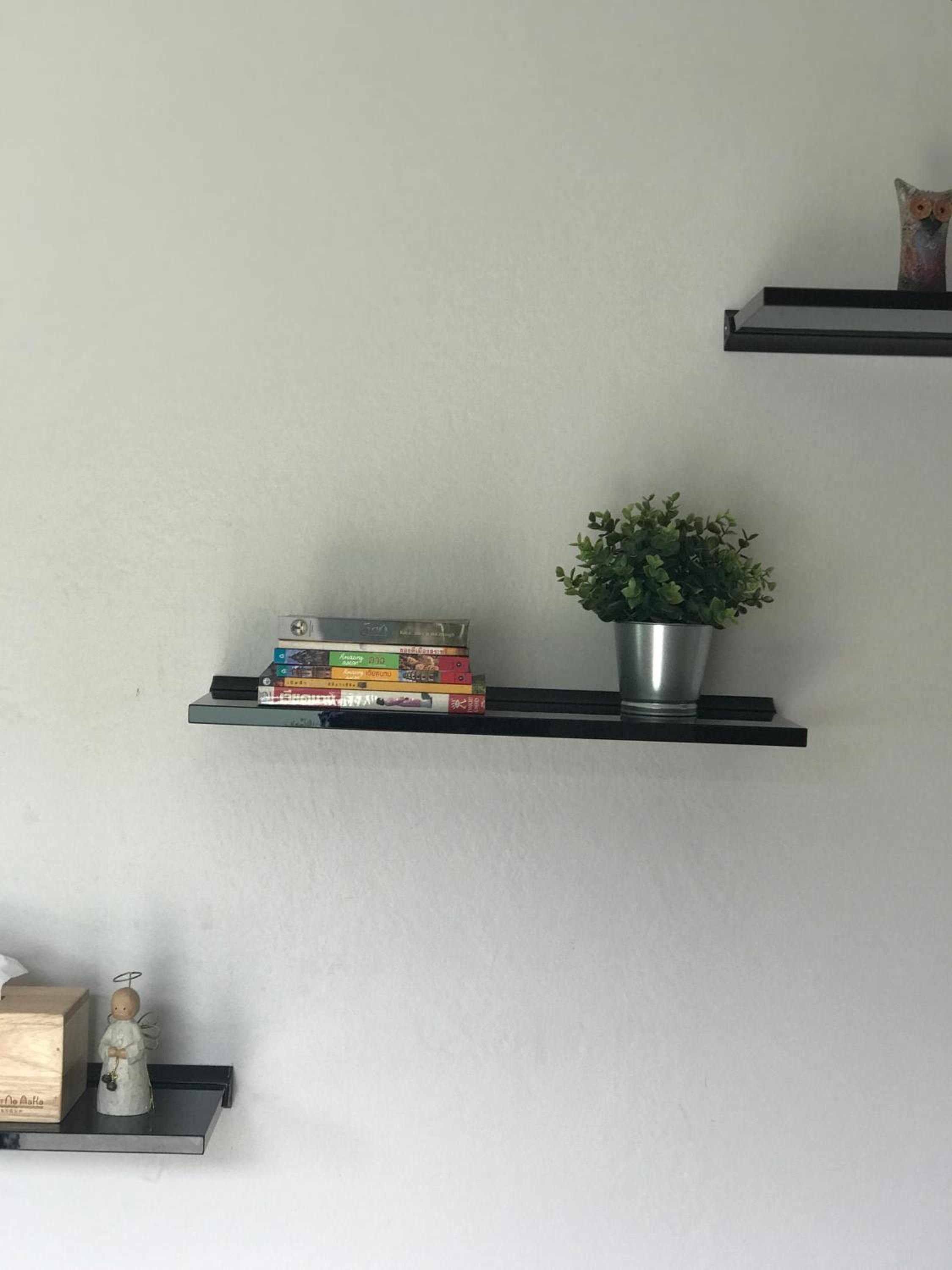 Una pared con tres estantes negros flotantes, cada uno con objetos diferentes.