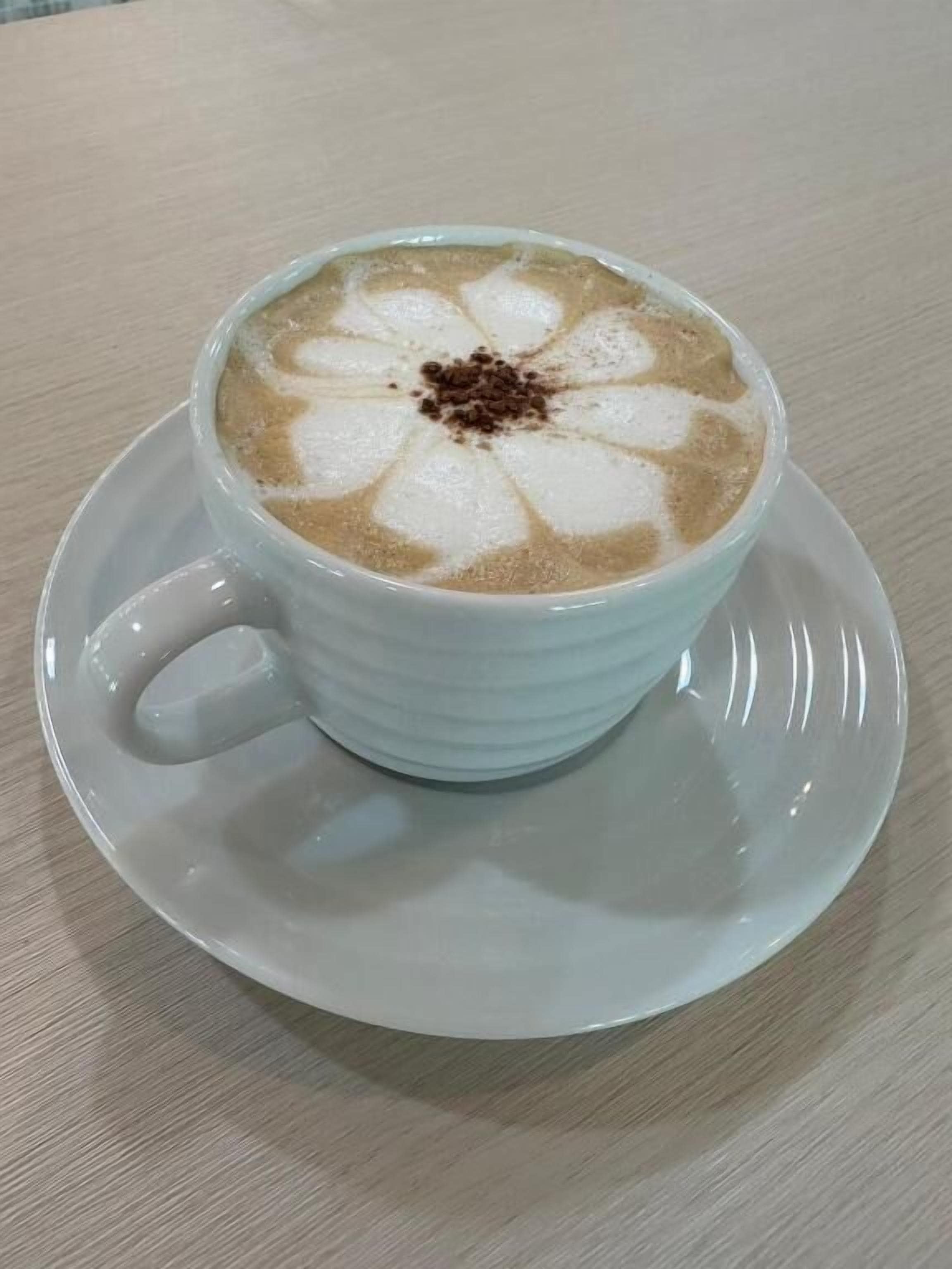 Una taza de café blanco con un diseño floral sobre un platito.