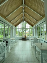 Una habitación amplia con techo alto, ventanas grandes y mobiliario blanco.