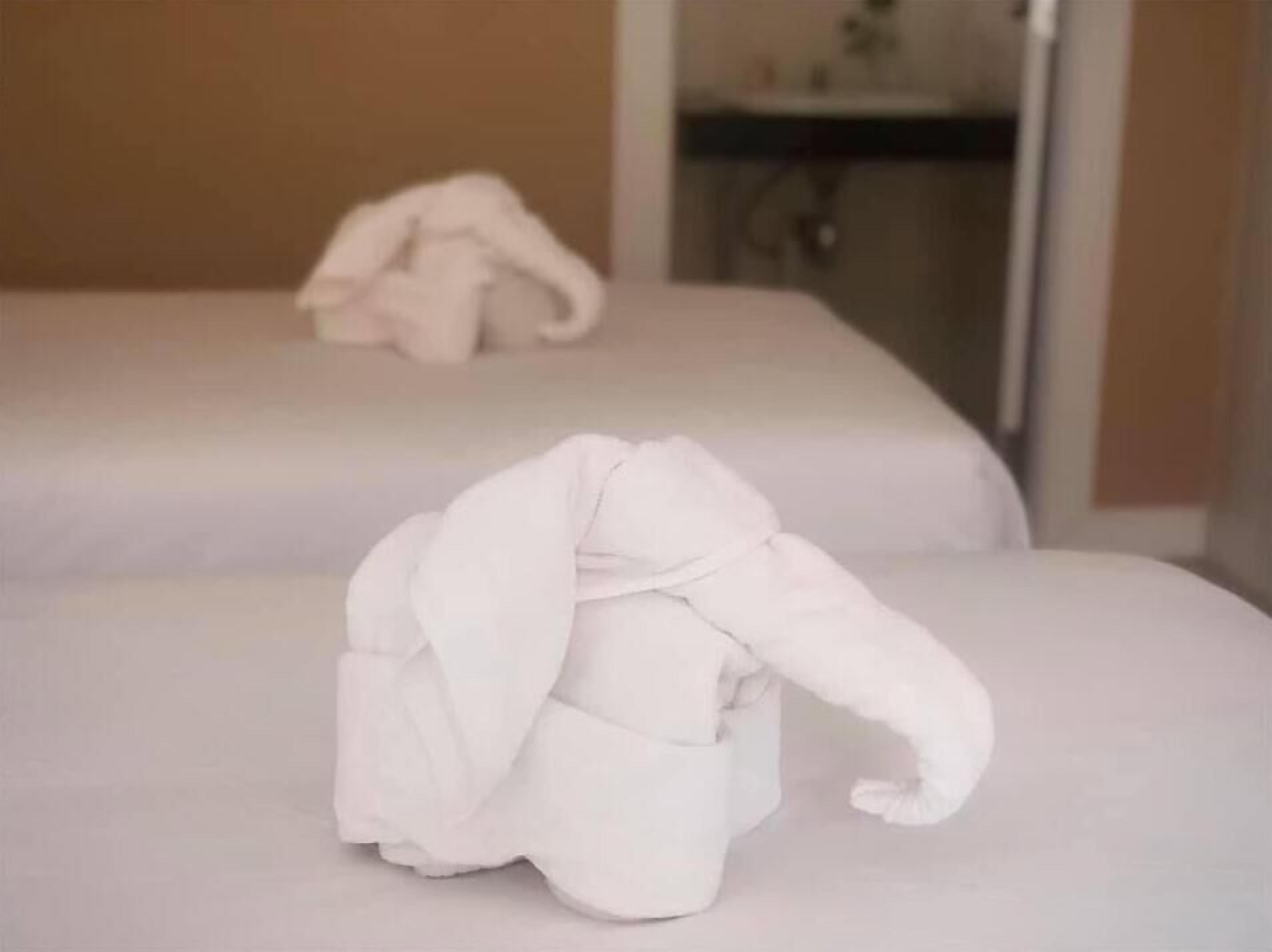 Two beds with white linens and a towel arranged in an elephant shape on the floor.