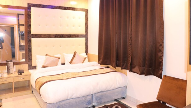 Ein Hotelzimmer mit einem großen Bett, einem Nachttisch, einem Spiegel und einem Fenster mit Vorhängen.
