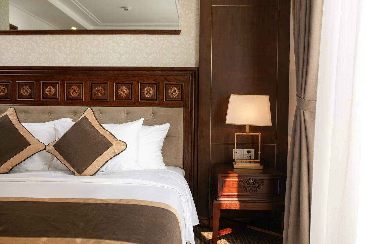 A hotel room with a large bed, a nightstand with a lamp, and a mirror above the bed.