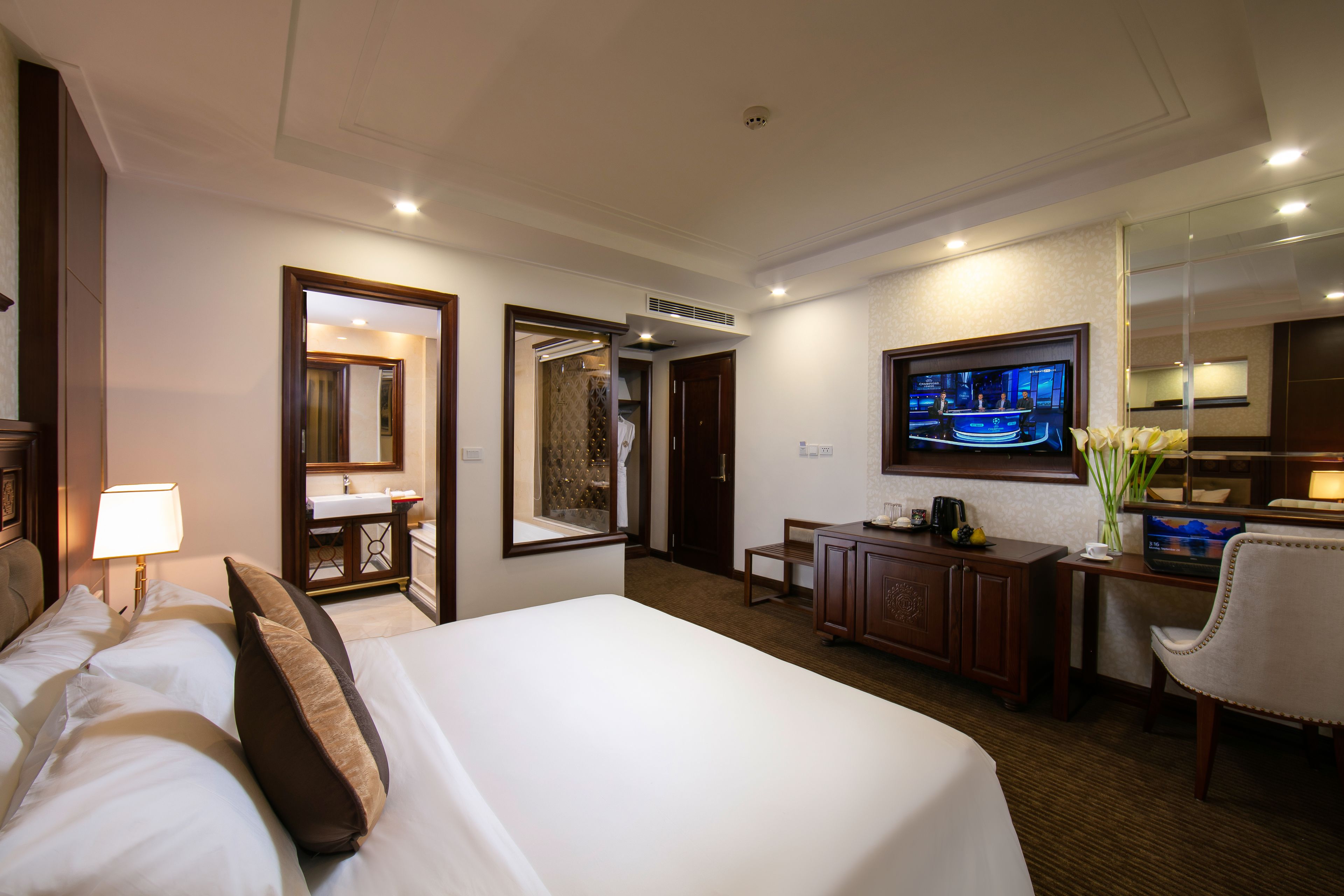 A hotel room with a large bed, a desk, a chair, a television, and a bathroom visible through an open door.