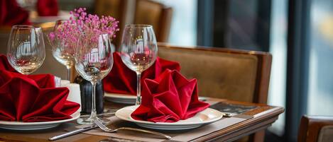 A dining table set with red napkins, clear wine glasses, and a vase with pink flowers.