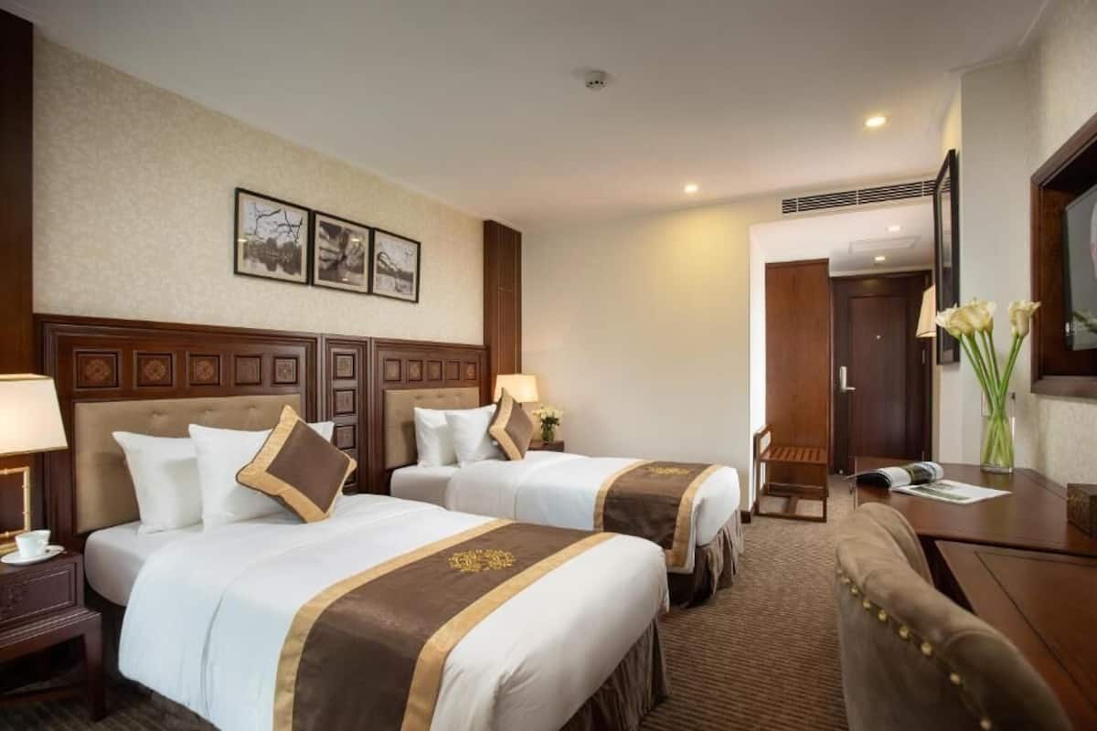 A hotel room with two beds, a desk, a chair, a TV, and a framed picture on the wall.