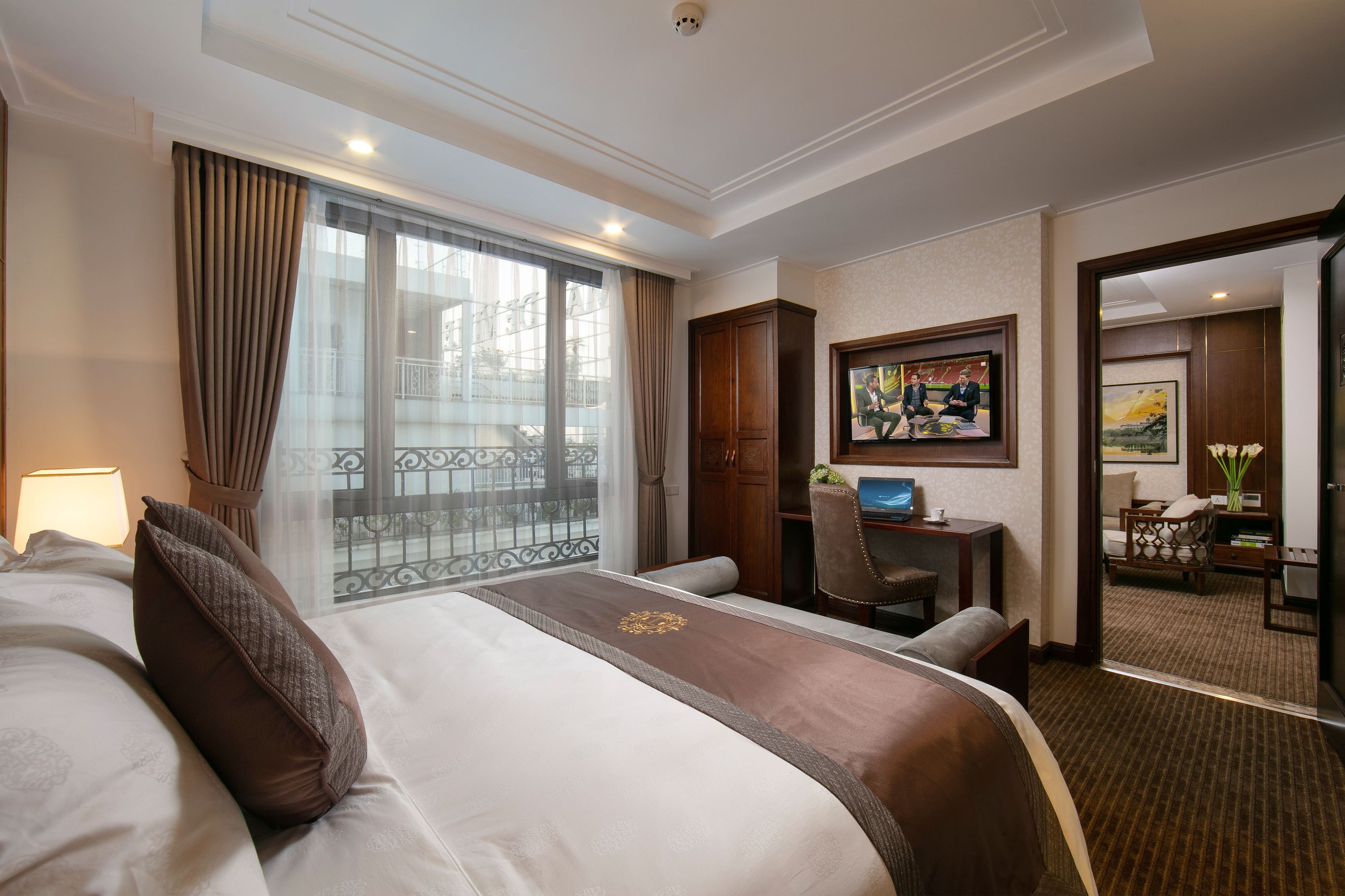 A hotel room with a large bed, a desk, a chair, and a view of the outside balcony.