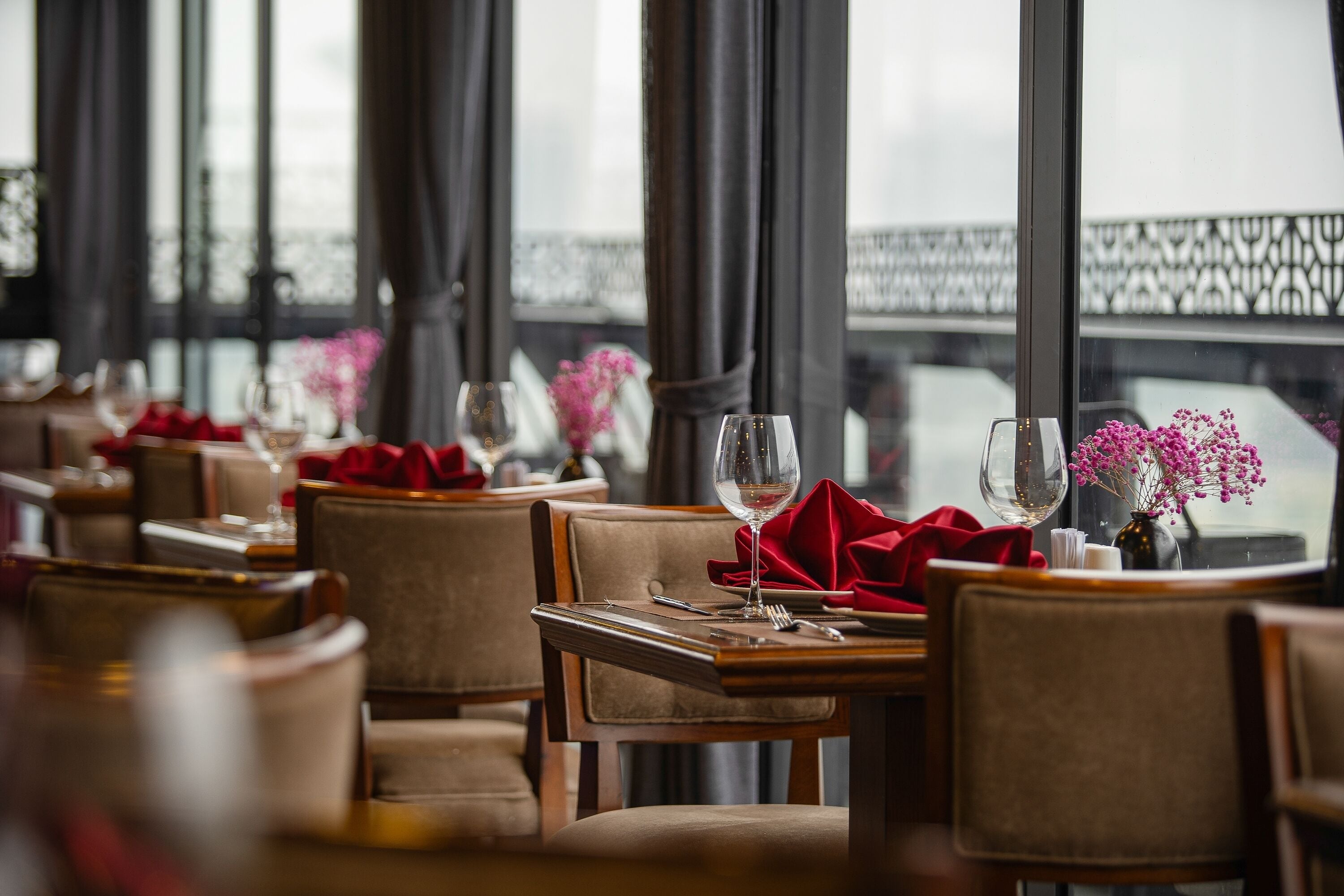 A restaurant with tables set for dining, featuring a view of a bridge through large windows.