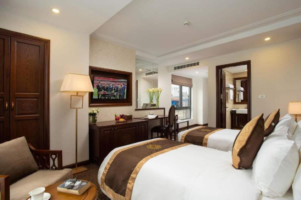 A hotel room with two beds, a desk, a chair, a TV, and a large mirror.