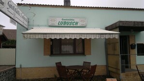 A small outdoor seating area with a table and chairs, a covered awning, and a sign indicating the establishment is open. - Restaurant Pension Lubusch Gahro (Crinitz)